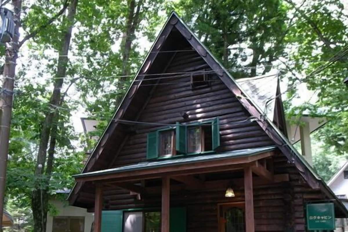 A rustic log cabin with a porch, a small table, and a chair.