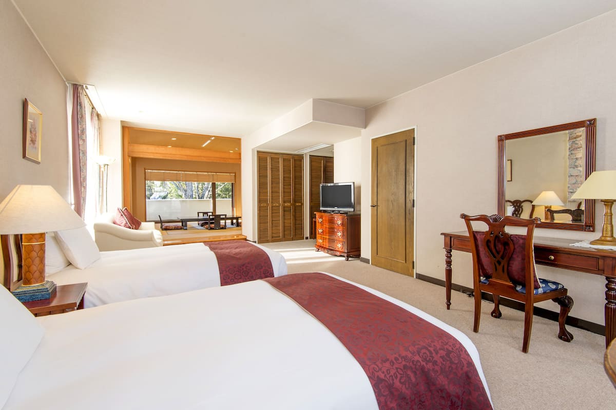 A hotel room with two beds, a desk, a chair, a television, and a mirror.