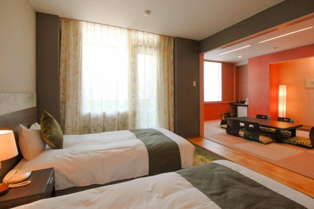 A hotel room with two beds, a desk, and a dining area.