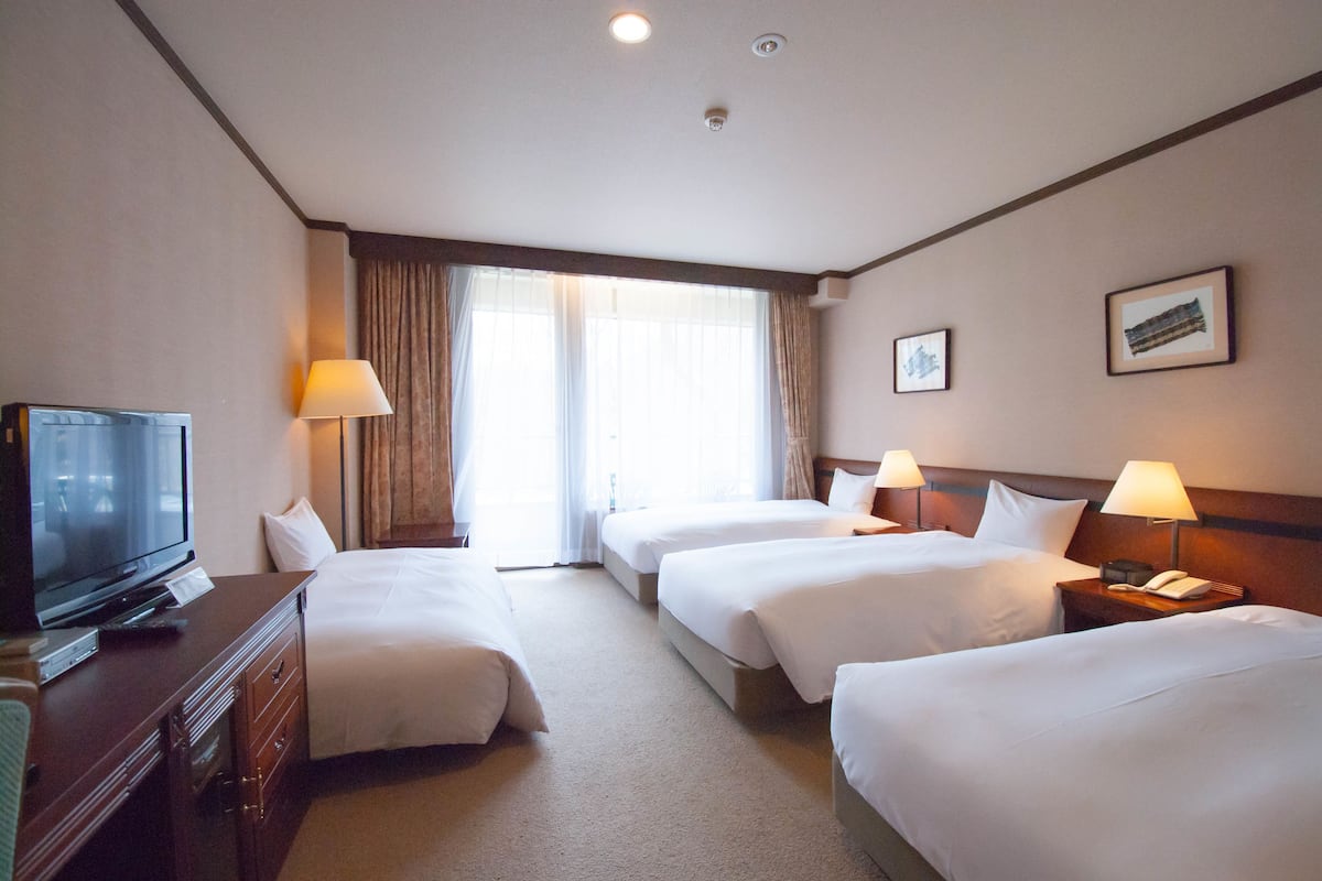 A hotel room with three beds, a television, and a desk with a lamp.