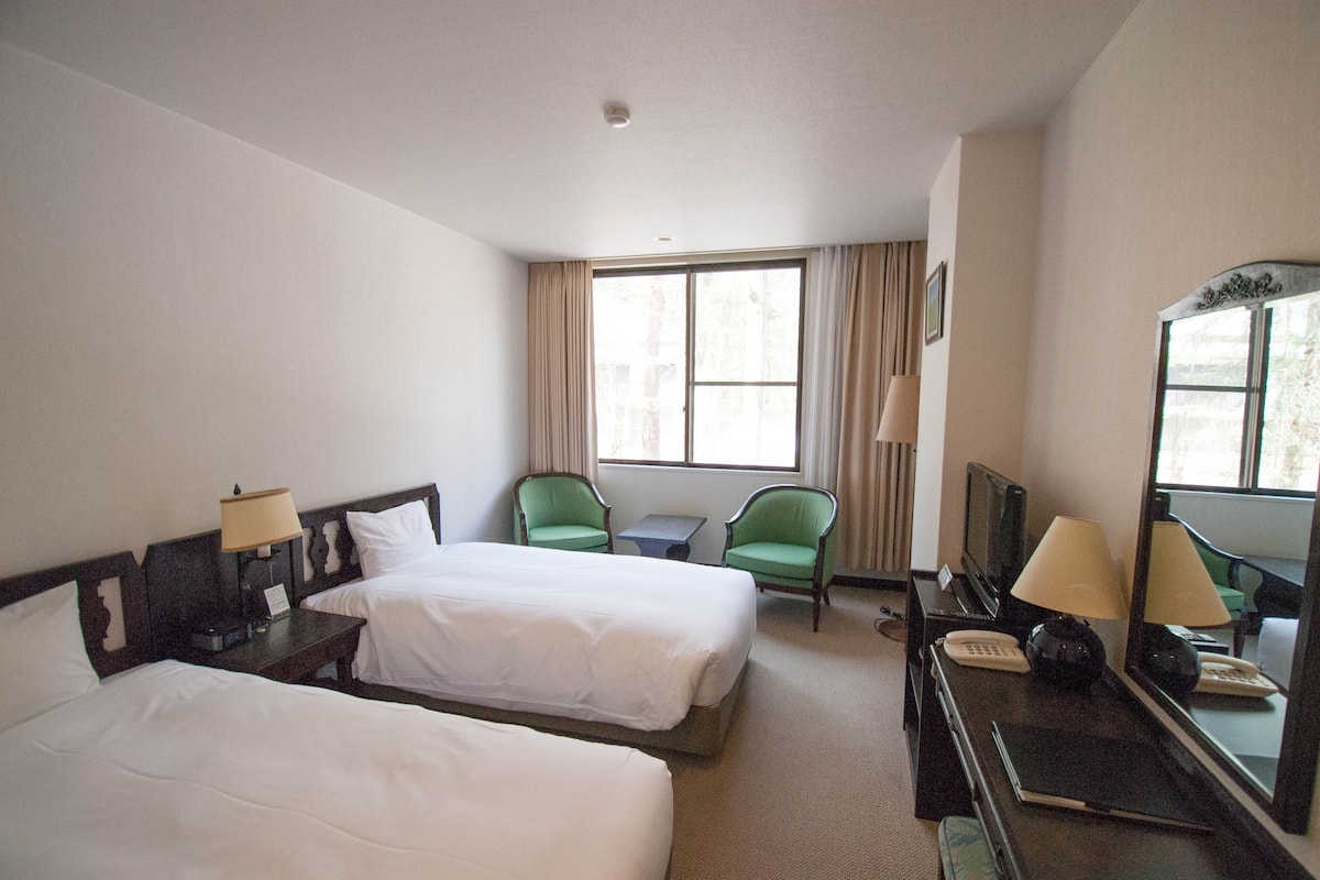 A hotel room with two beds, a desk with a lamp, a chair, a television, and a mirror.