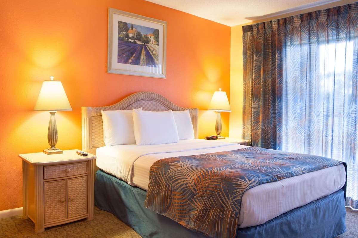 A hotel room with a bed, two bedside lamps, a nightstand, and a painting on the wall.