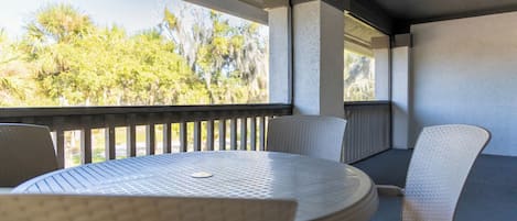 Un espace extérieur aménagé, abrité et doté d’une table ronde et de quatre chaises, offrant une vue sur des arbres et un bâtiment.