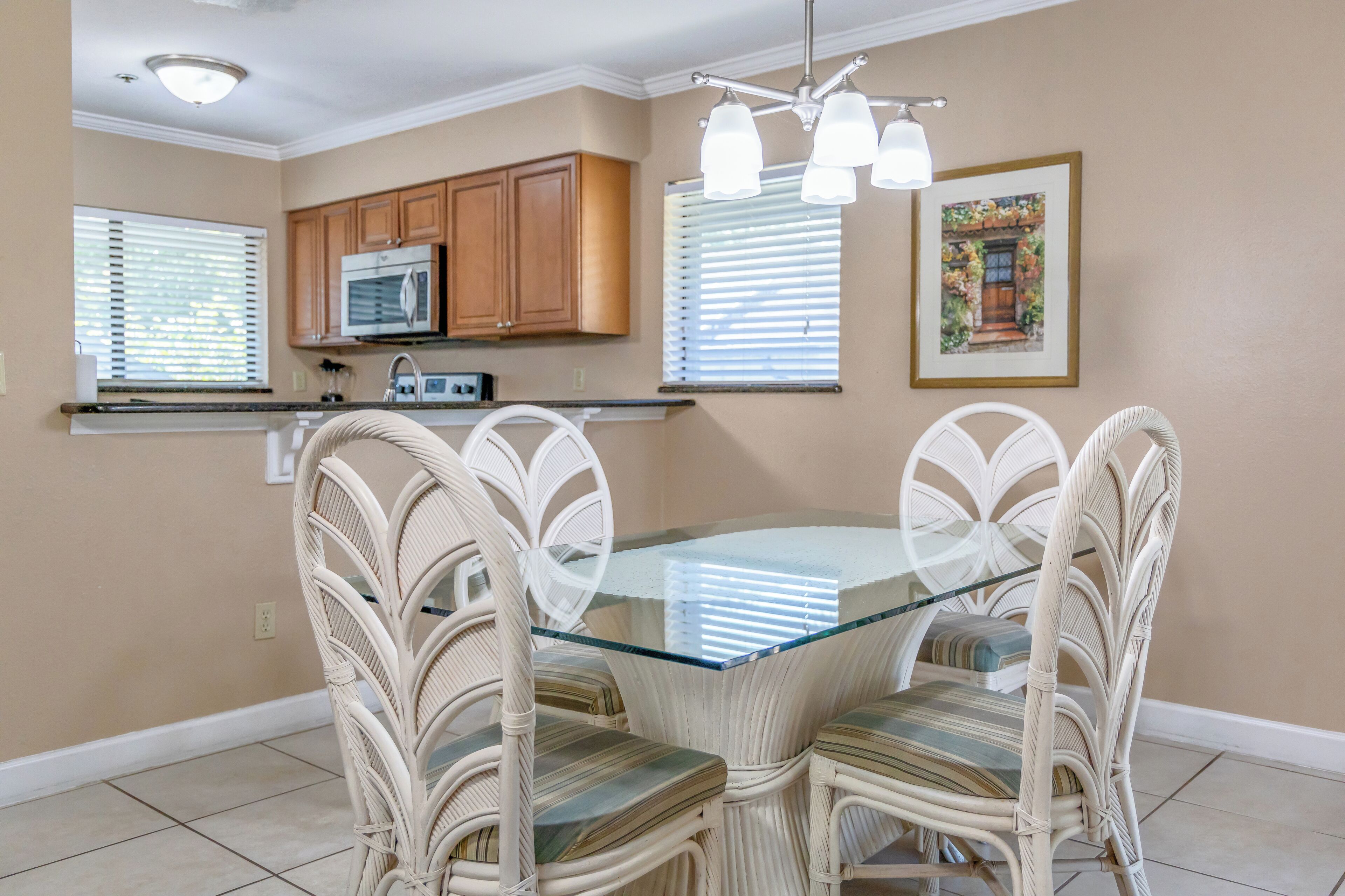 A dining area with a glass-top table surrounded by wicker chairs, wooden cabinets above, and a ceiling light fixture.