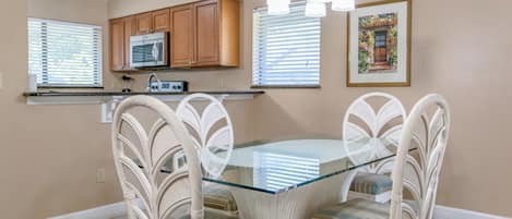 A dining area with a glass-top table surrounded by wicker chairs, wooden cabinets above, and a ceiling light fixture.