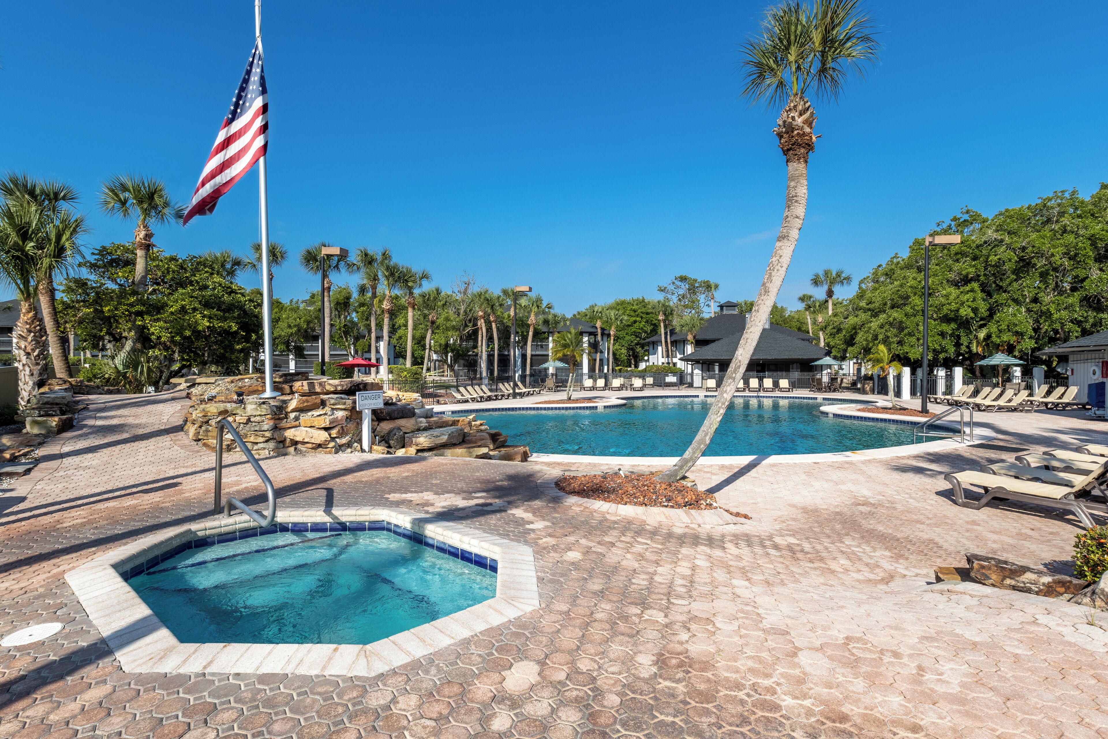 Zona de piscina con dos piscinas, palmeras y una bandera.