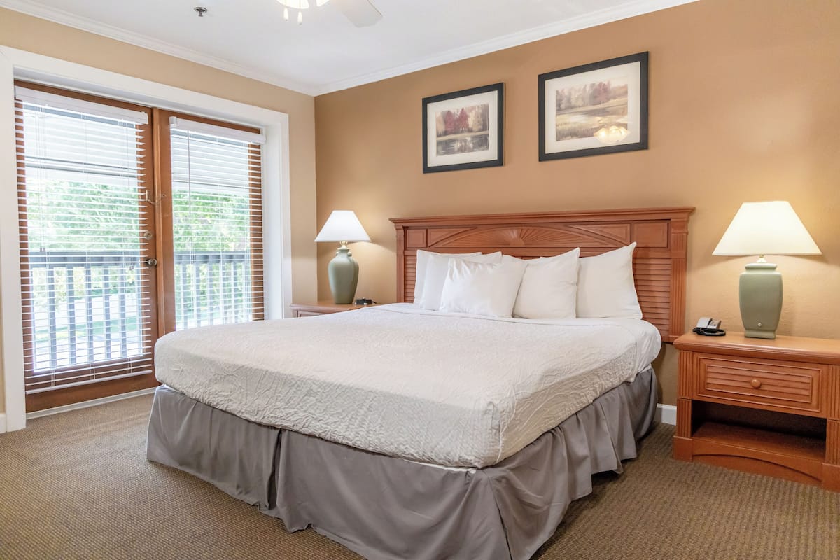 A neatly arranged bedroom with a large bed, two bedside lamps, and a view through a sliding door to an outdoor area.