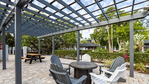 Une terrasse extérieure avec des fauteuils Adirondack, une table ronde et une structure en forme de pergola.