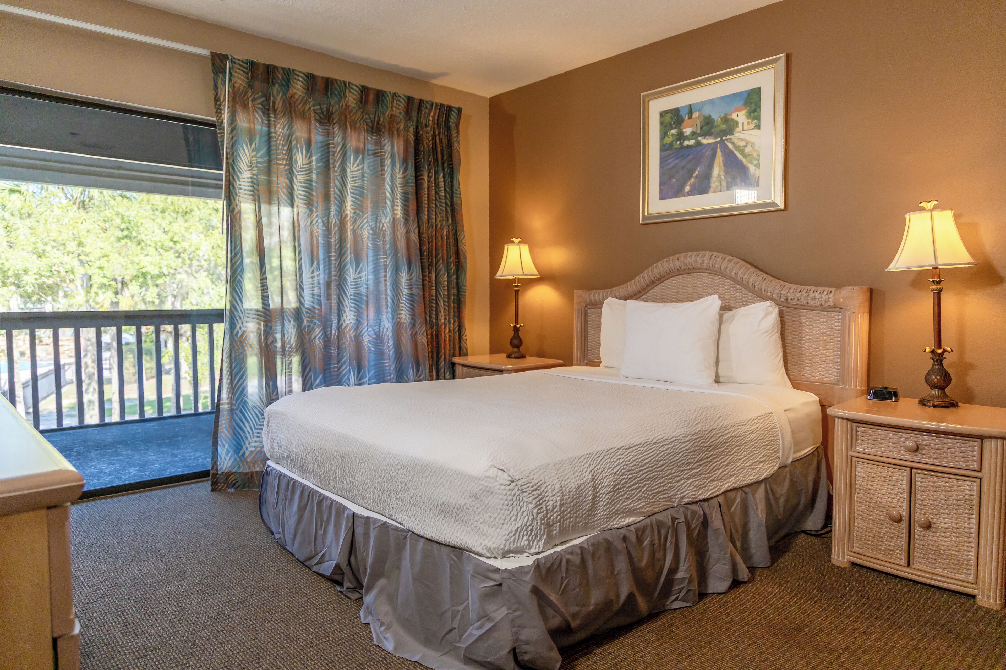 A hotel room with a large bed, two bedside tables with lamps, a window with curtains, and a painting on the wall.