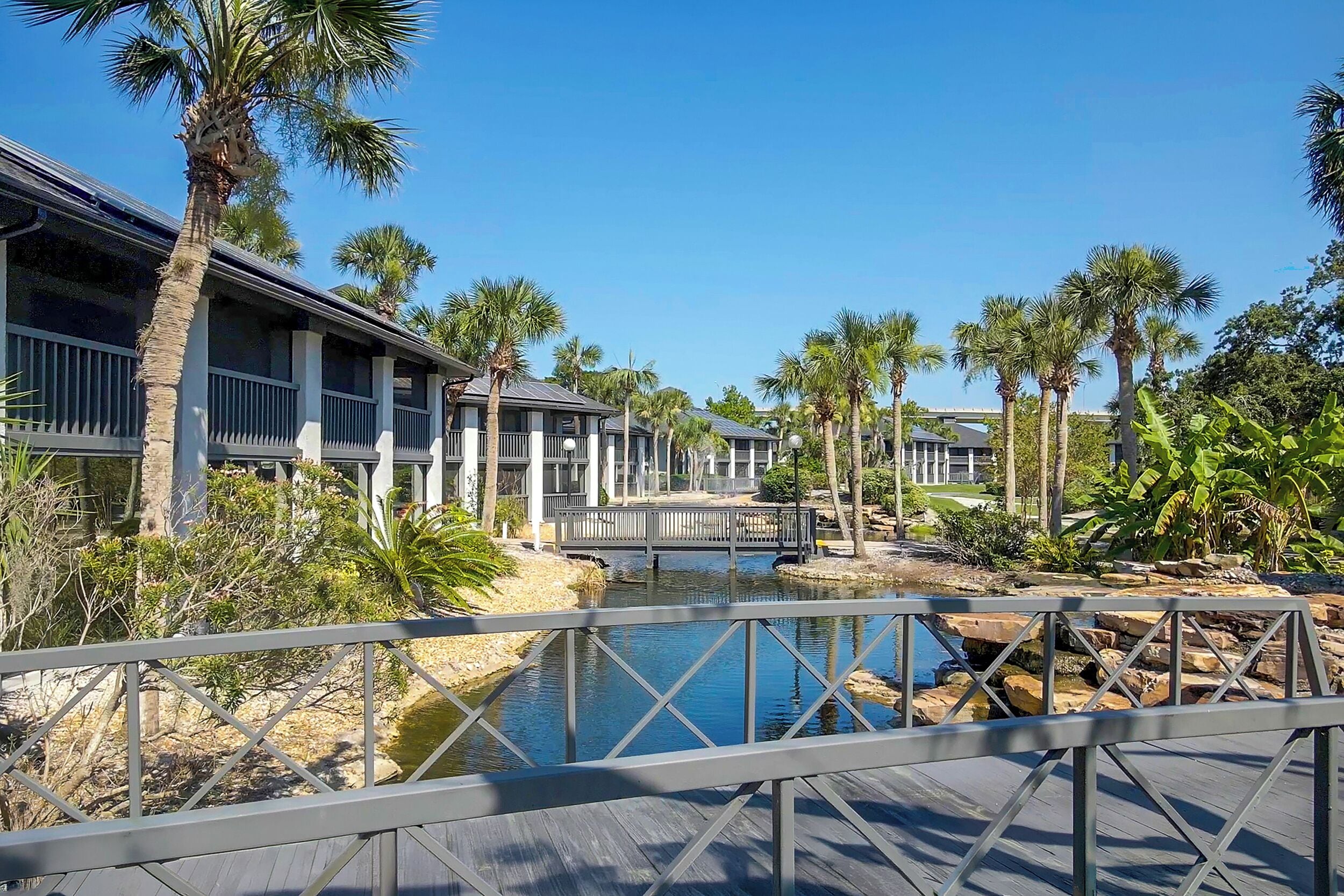 A resort with multiple buildings, a bridge, a water feature, and palm trees.