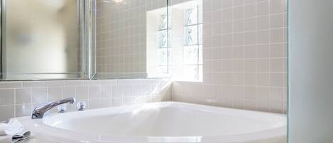 A modern bathroom with a large bathtub, a glass shower enclosure, and a mirror above the sink.