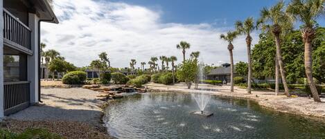 A serene outdoor area with a pond, palm trees, and a building with a balcony.