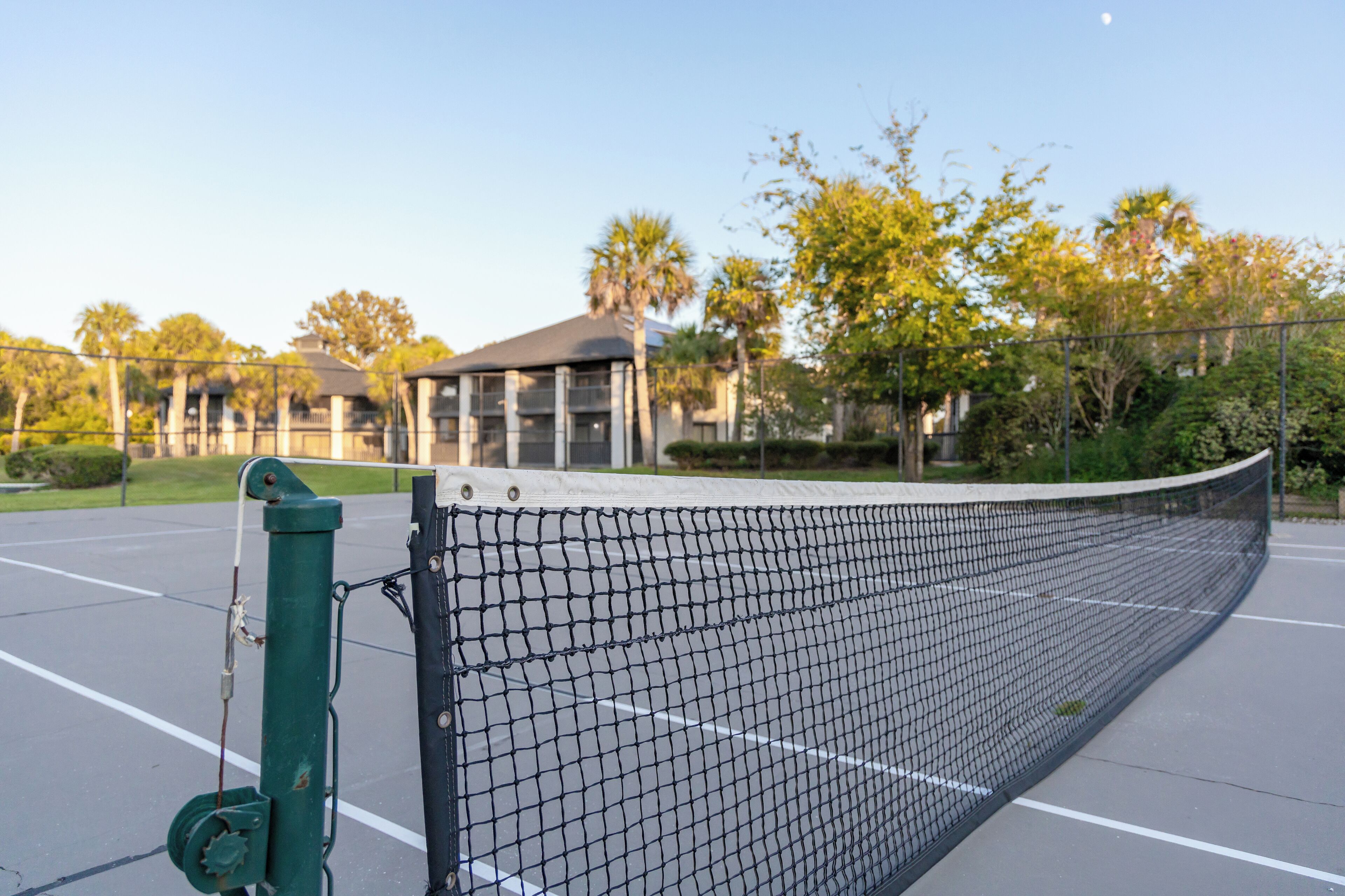 A tennis court with a net, surrounded by a fence and trees.