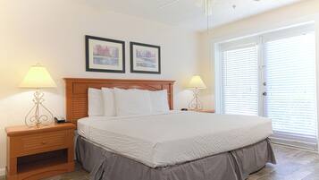A bedroom with a large bed, two bedside tables with lamps, a ceiling fan, and two framed pictures on the wall.