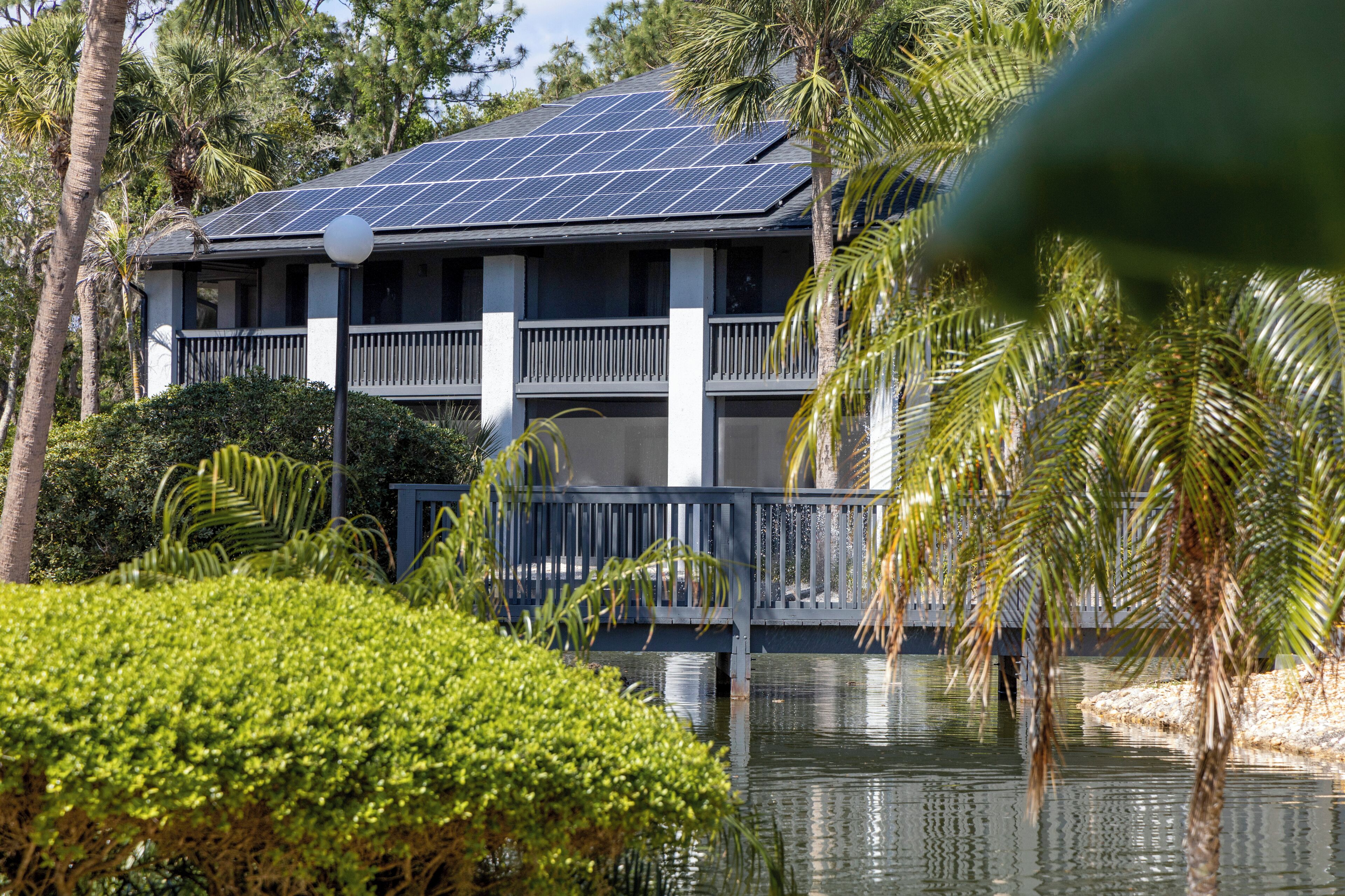 A two-story building with a balcony, surrounded by lush greenery and a body of water.