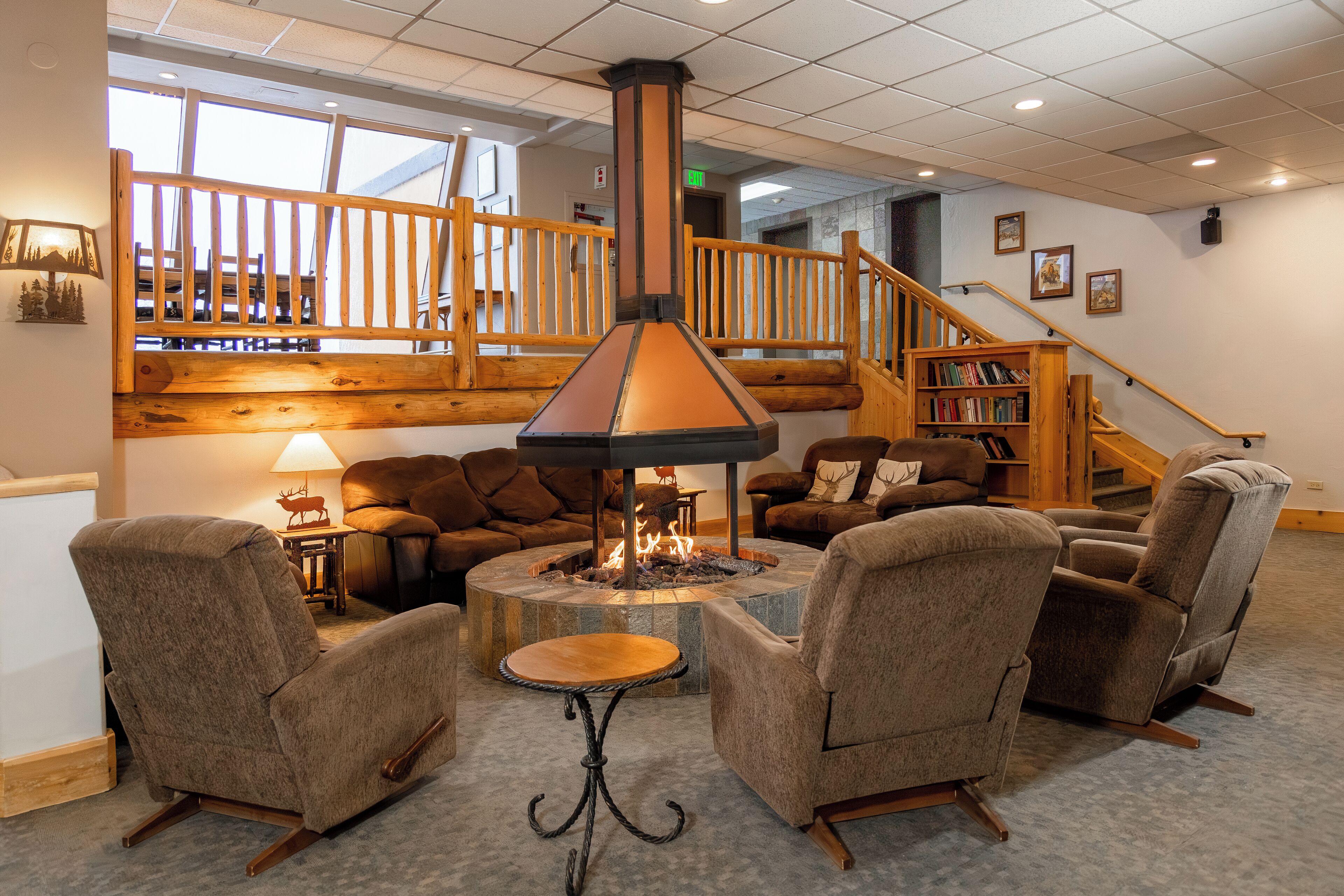 A cozy lounge area with a stone fire pit, comfortable seating, and a staircase with wooden railings.