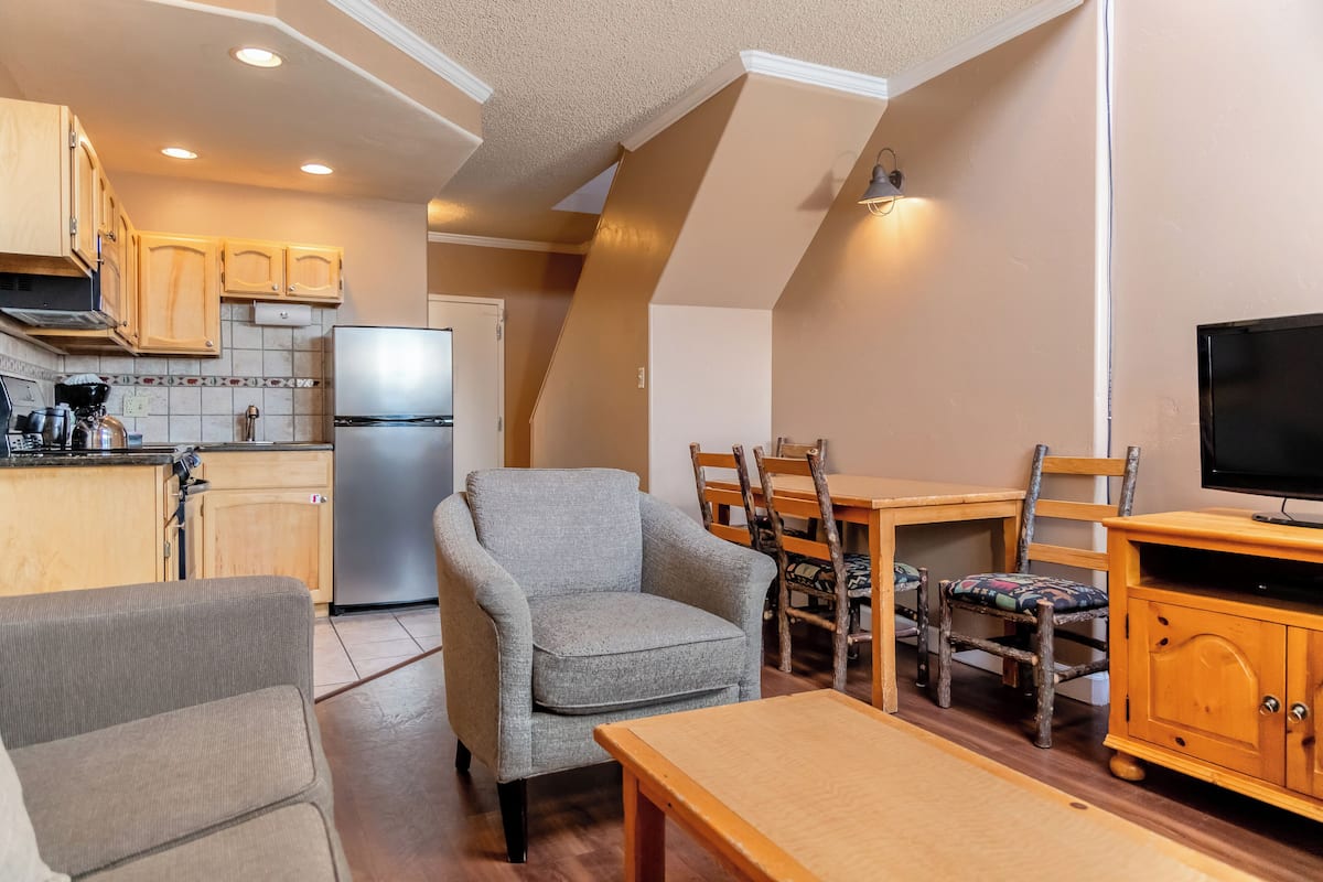 A compact kitchen with a refrigerator, wooden cabinets, and a dining area with a table and chairs.