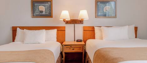 A hotel room with two beds, a nightstand with a lamp, and framed artwork on the wall.