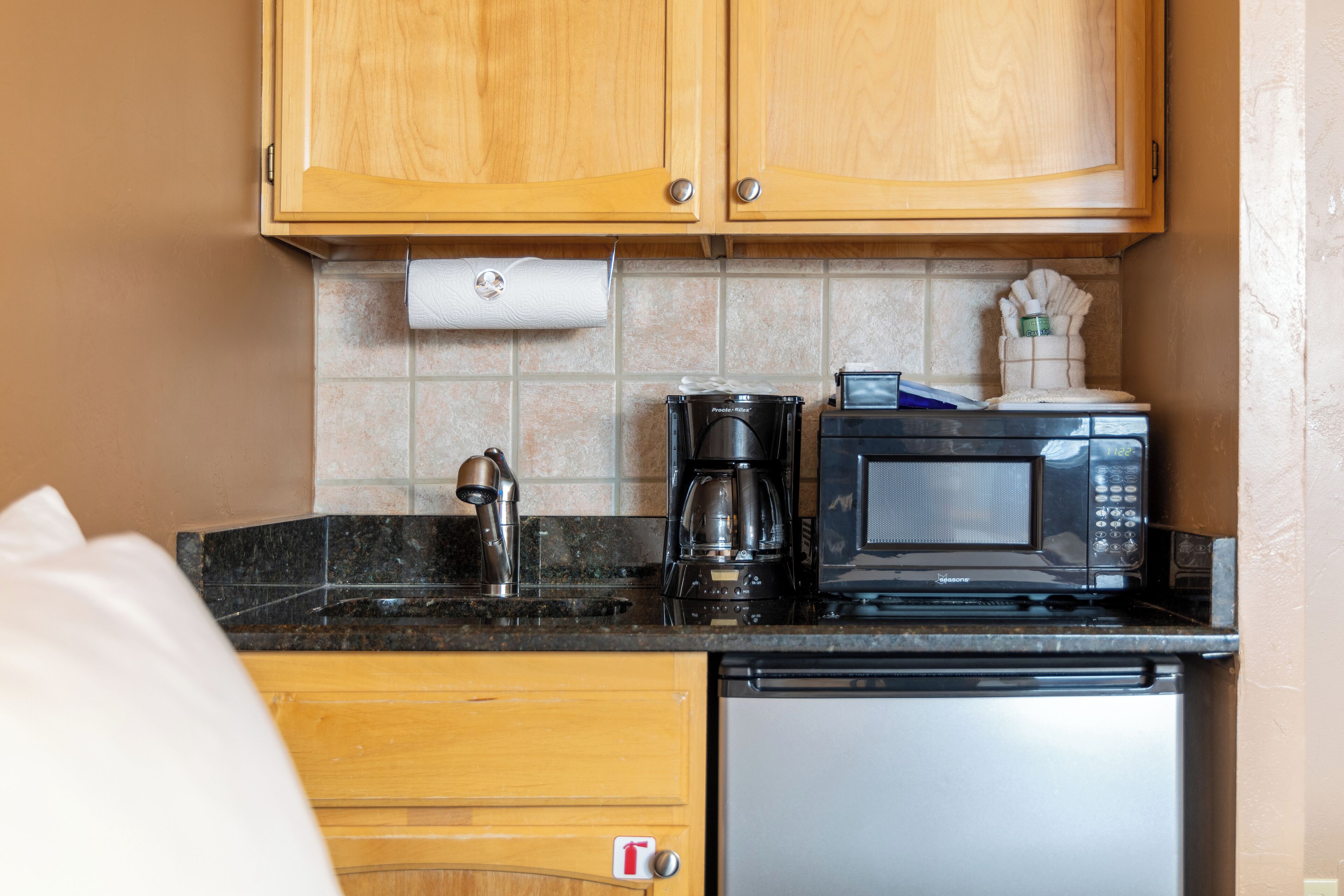 Una cocina compacta con armarios de madera, cafetera, microondas y lavavajillas.