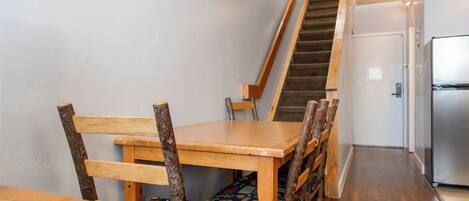 Une table à manger en bois avec des chaises, un escalier, un réfrigérateur et une porte dans un couloir.