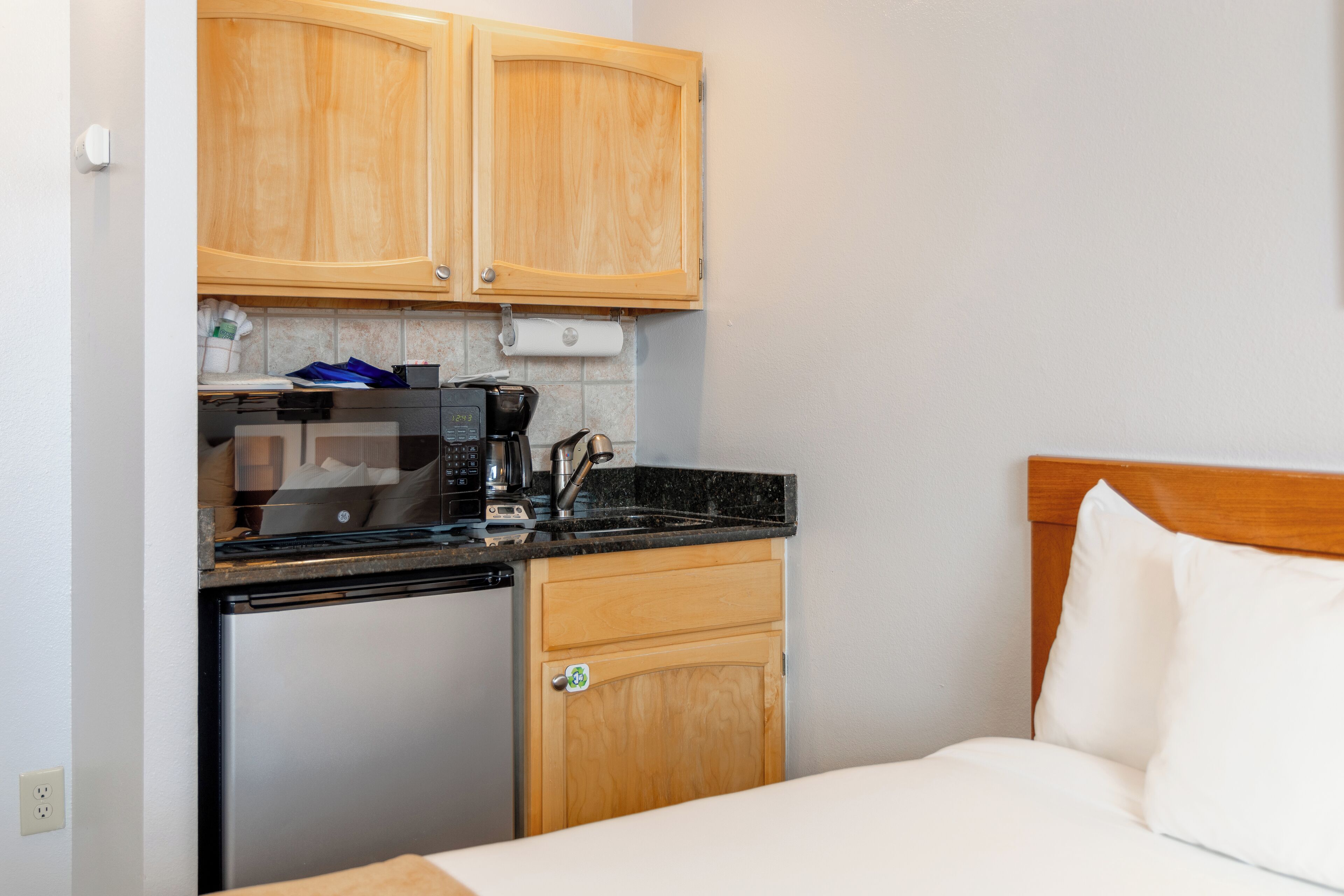A compact kitchenette with wooden cabinets, a coffee maker, and a refrigerator.