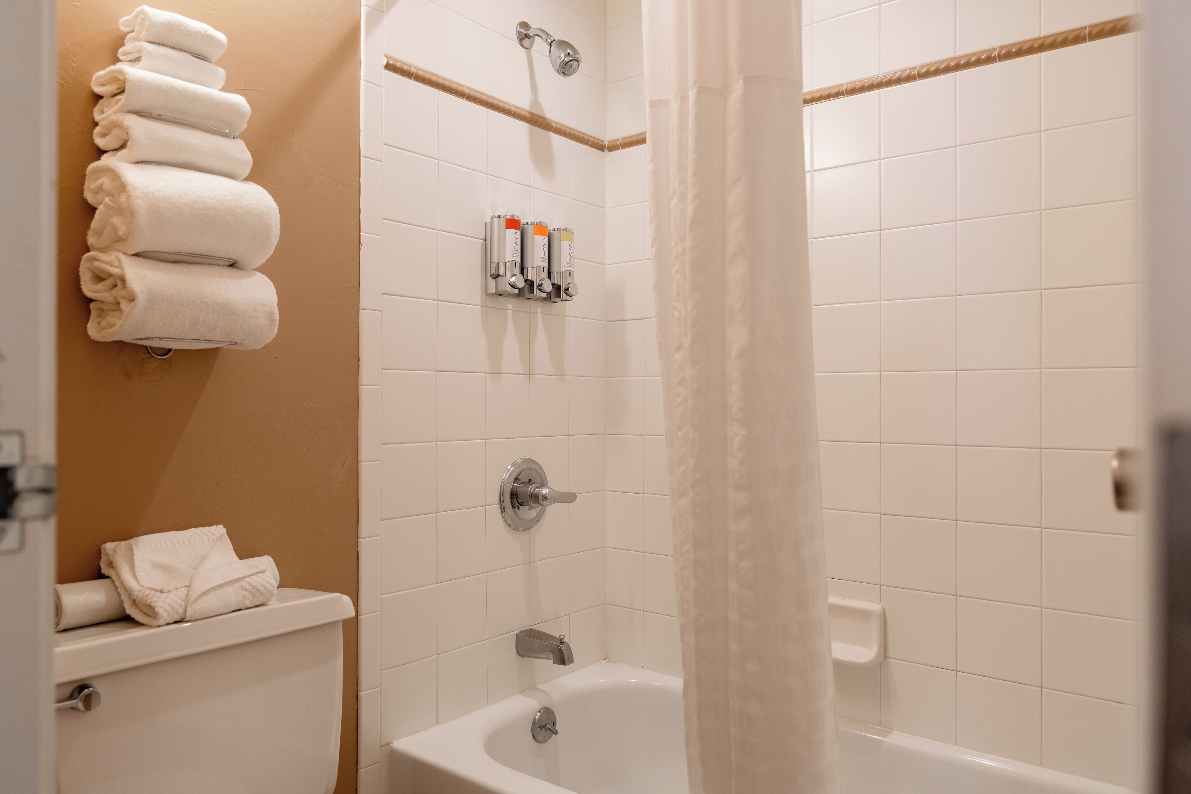Ein Badezimmer mit einer weißen Badewanne, einer Duschkabine mit Vorhang und einem Handtuchhalter mit gefalteten Handtüchern.