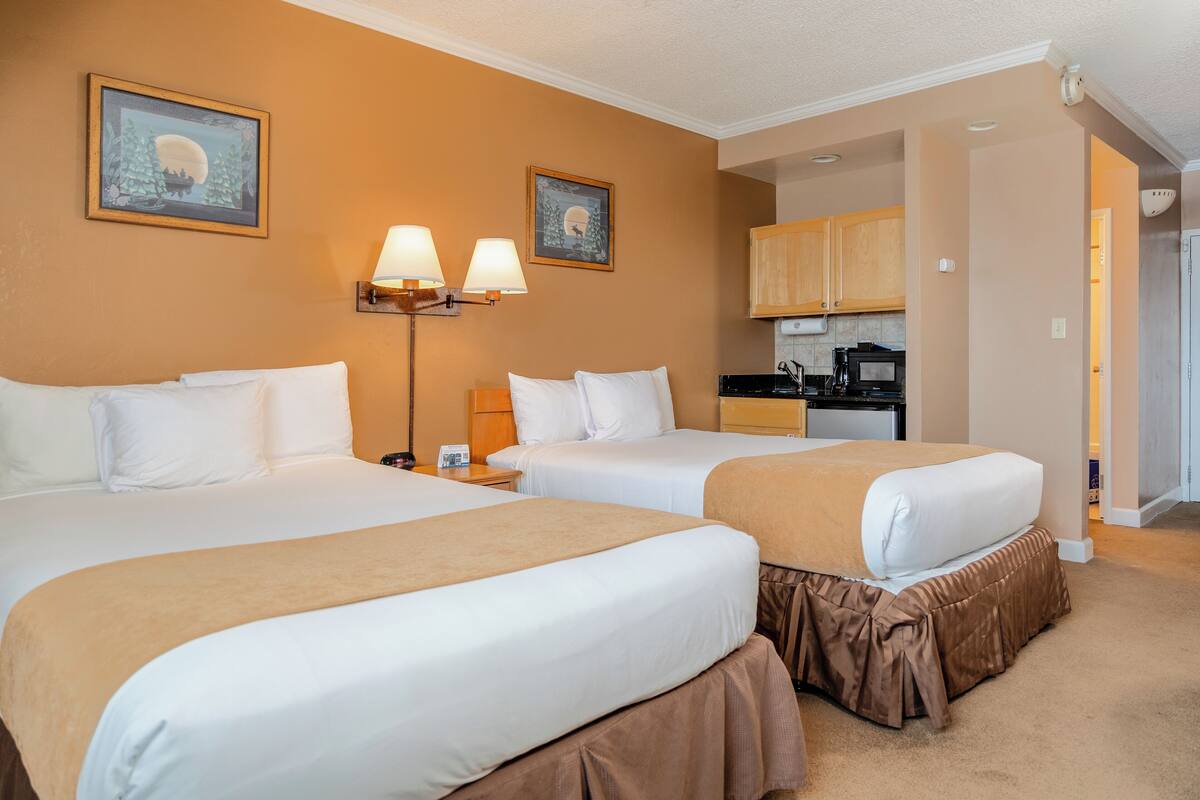 A hotel room with two beds, a kitchenette, and a dining area.