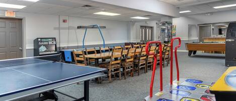 A room with a ping pong table, chairs, a pool table, and a dance floor.