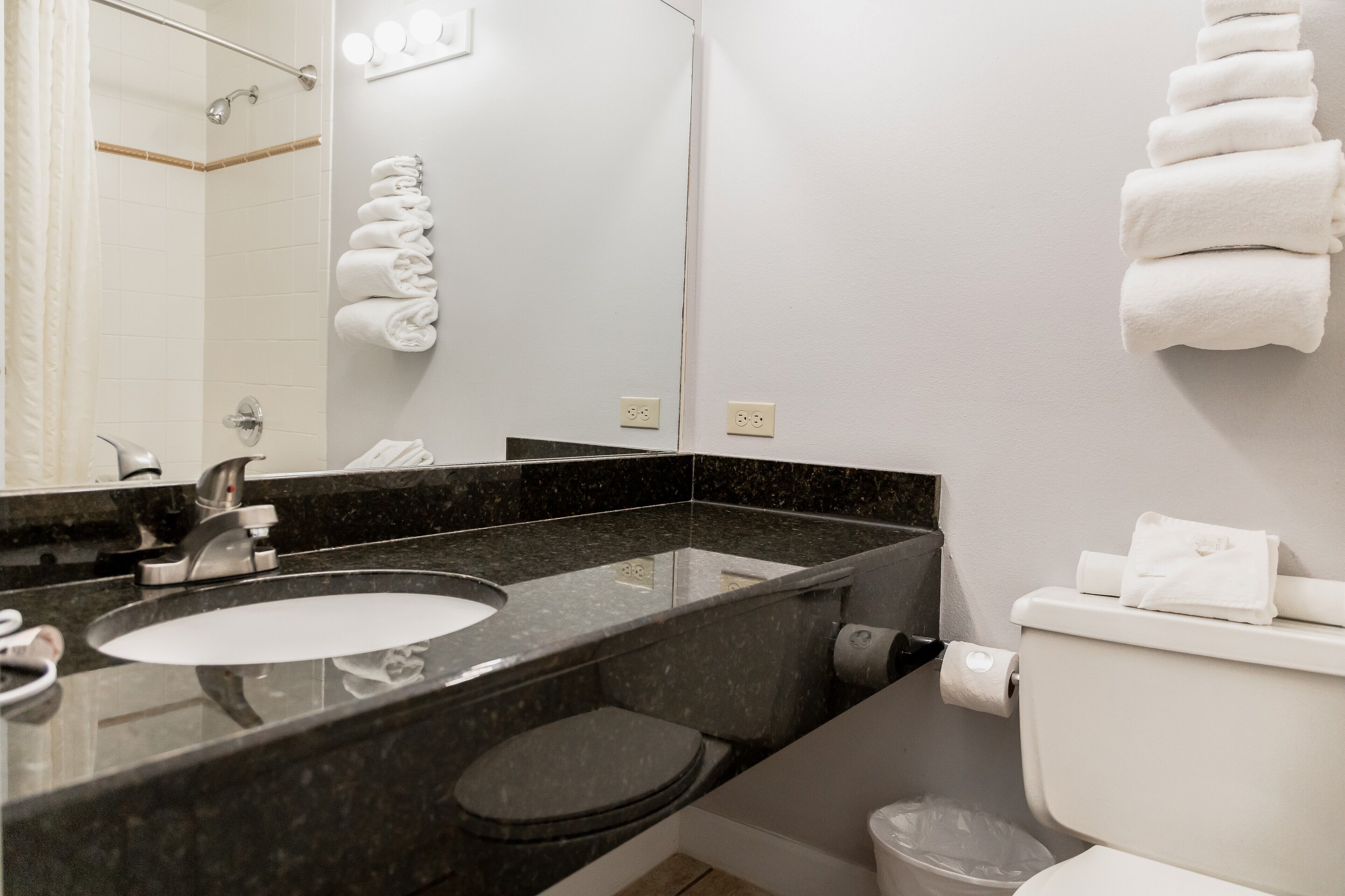 Un baño con lavamanos de mármol negro, inodoro blanco y toallero con toallas dobladas.