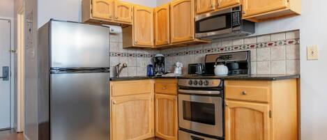 A kitchen with wooden cabinets, a stainless steel refrigerator, a microwave, a stove, and a tiled backsplash.