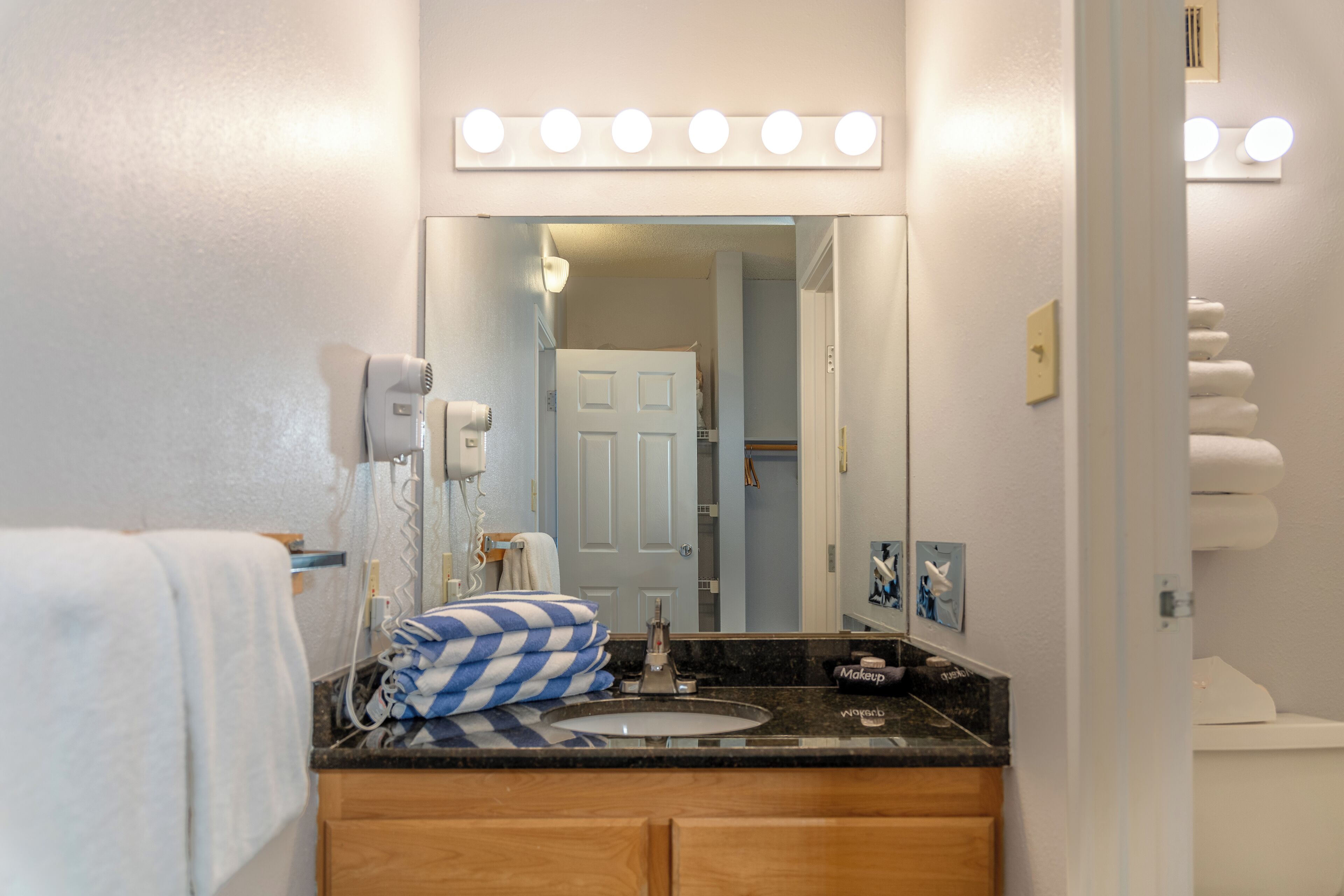 A bathroom with a sink, mirror, and vanity. There are lights above the mirror and a towel rack.