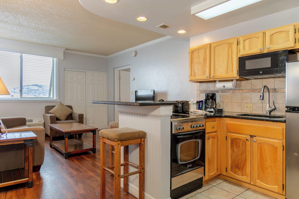 A compact kitchen with wooden cabinets, a microwave, an oven, and a coffee maker.