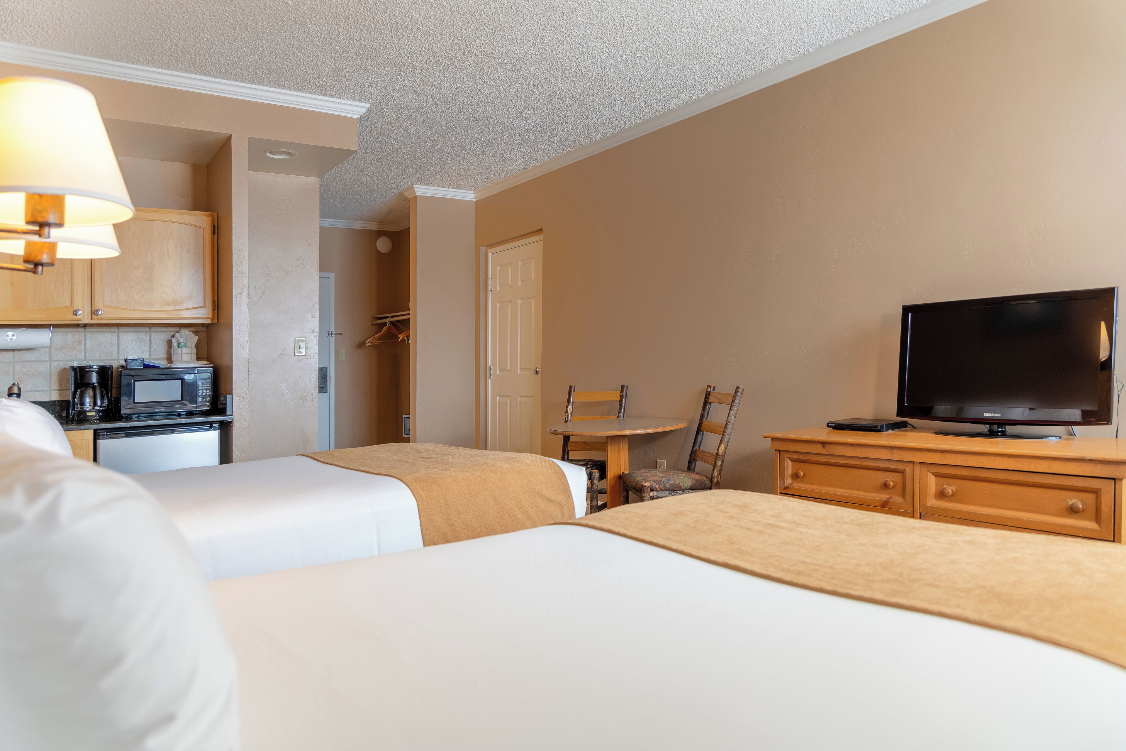 A hotel room with two beds, a dining table, a TV, a microwave, and a coffee maker.
