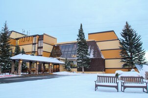 Un hotel con entrada cubierta de nieve, mobiliario exterior y una amplia fachada de vidrio.