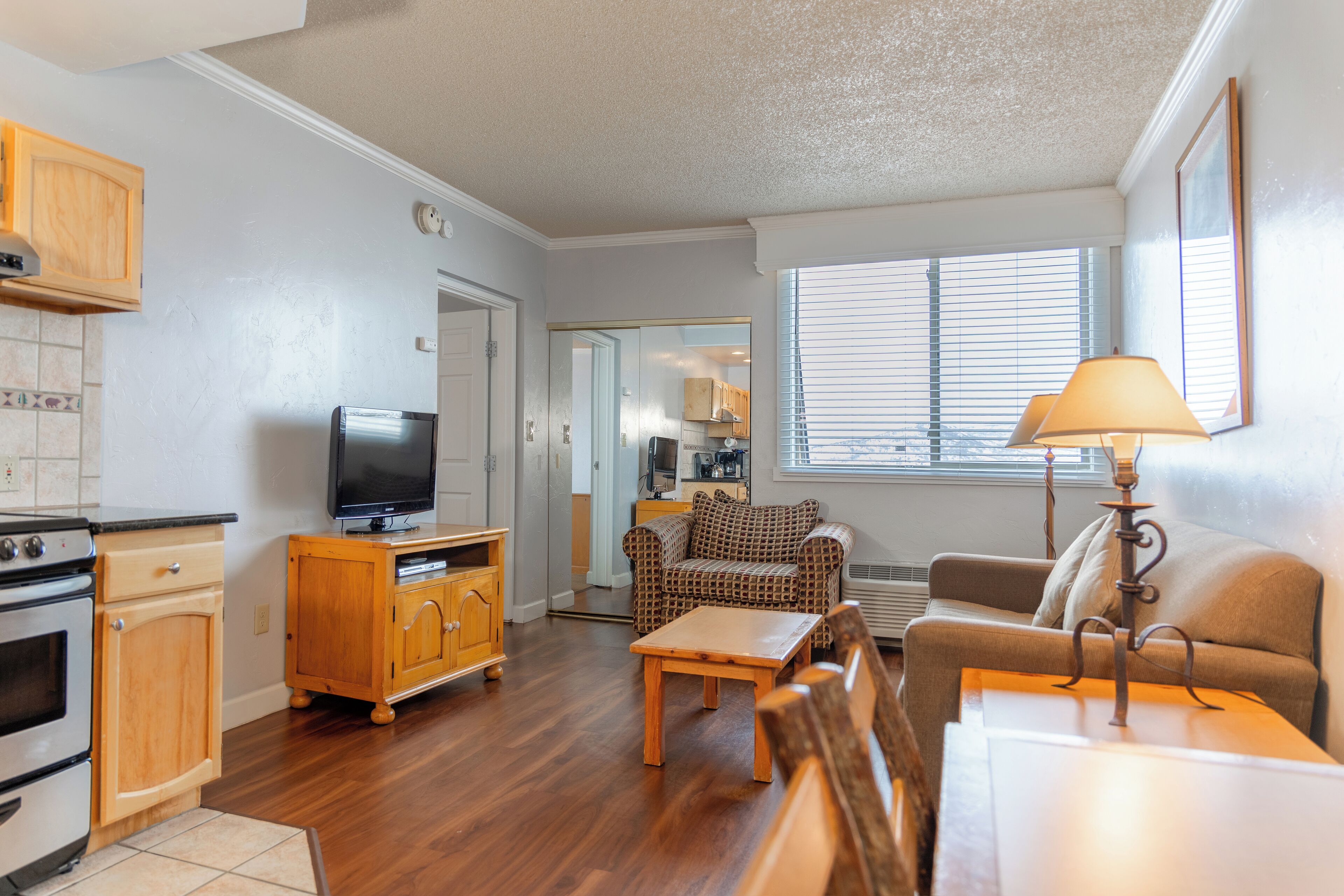 A compact living space with a kitchenette, a television, a sofa, a coffee table, and a lamp.