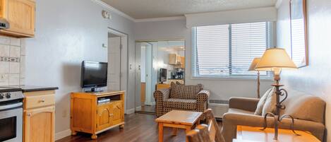 A compact living space with a kitchenette, a television, a sofa, a coffee table, and a lamp.