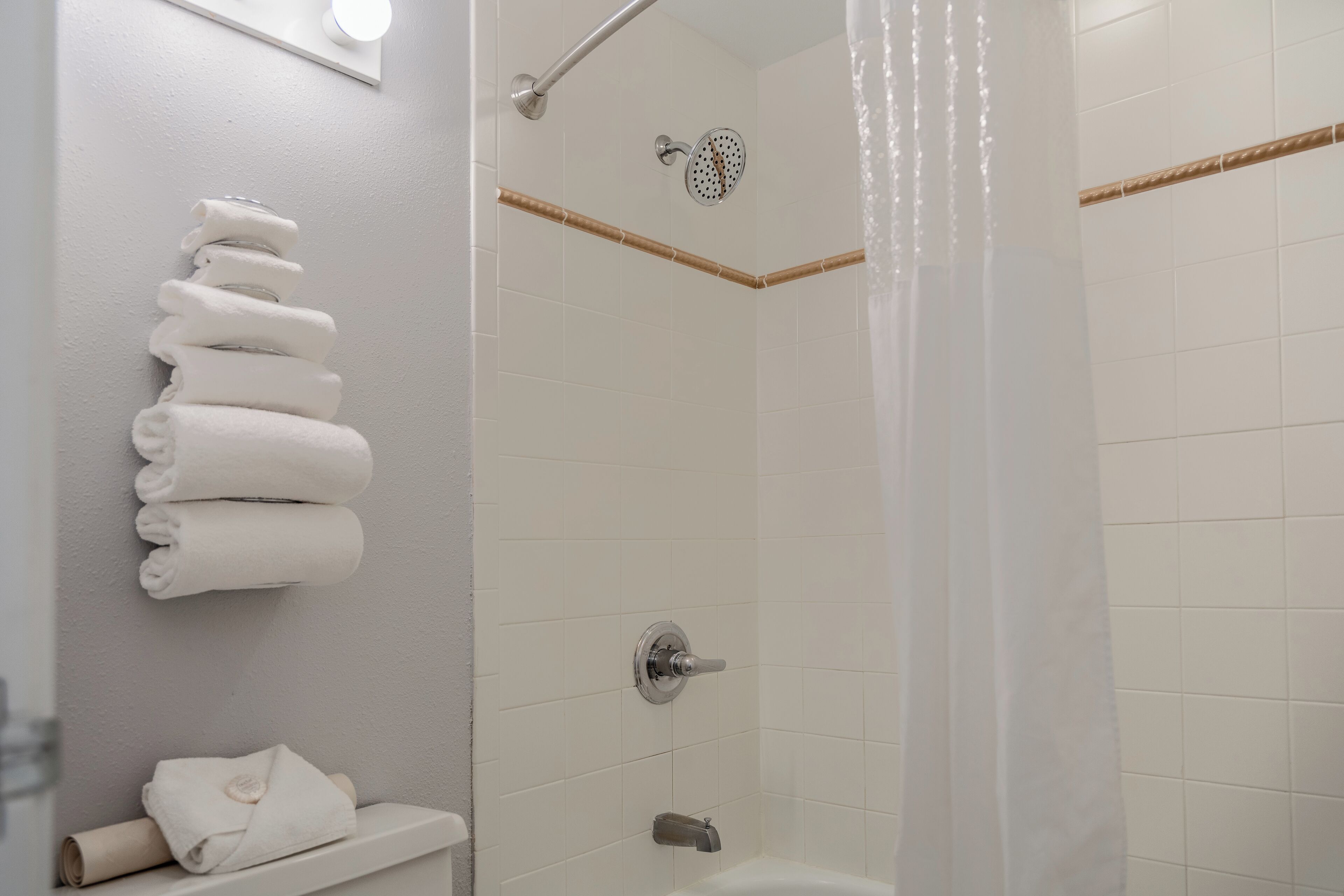 A bathroom with a shower, a toilet, and a stack of neatly folded towels on the wall.