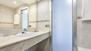 Un baño moderno con encimera de mármol, un lavabo, un espejo y una cabina de ducha de vidrio.