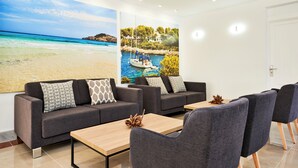 Una sala de estar moderna con sofás grises, una mesa de centro de madera y un gran mural de playa y lago en la pared.