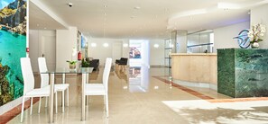 A modern hotel lobby with a reception desk, seating area, and a large mural. - Globales Torrenova Adults Only +16 (Calvia)