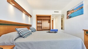Habitación de hotel con cama, cabecera de madera, armario, un cuadro y una mesita de noche.