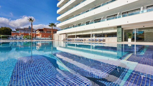 Una piscina con agua cristalina, sillas de descanso y un edificio moderno con balcones.