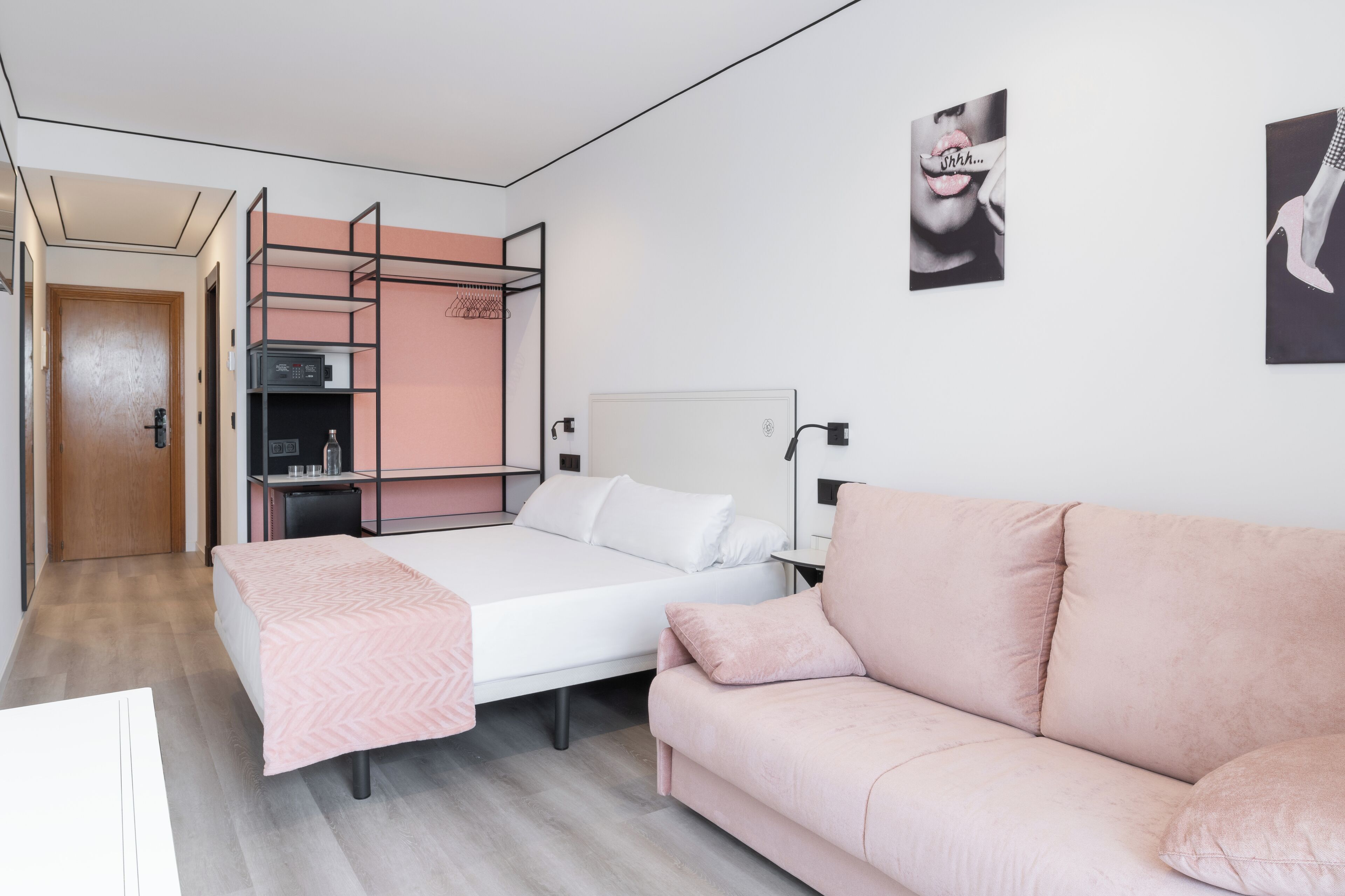 A bedroom with a bed, a pink sofa, a wardrobe, and a desk.