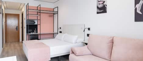 A bedroom with a bed, a pink sofa, a wardrobe, and a desk.