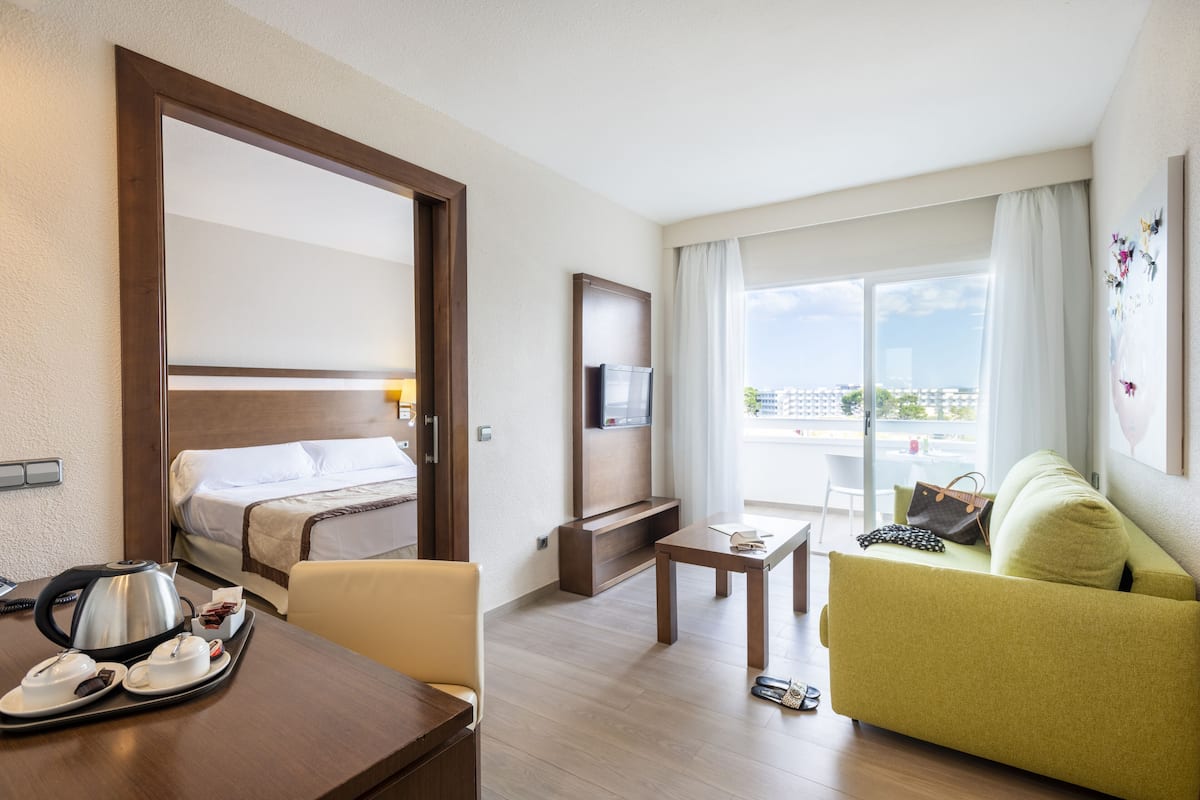 A hotel room with a bed, a TV, a sofa, a table, and a window with a view of the city.