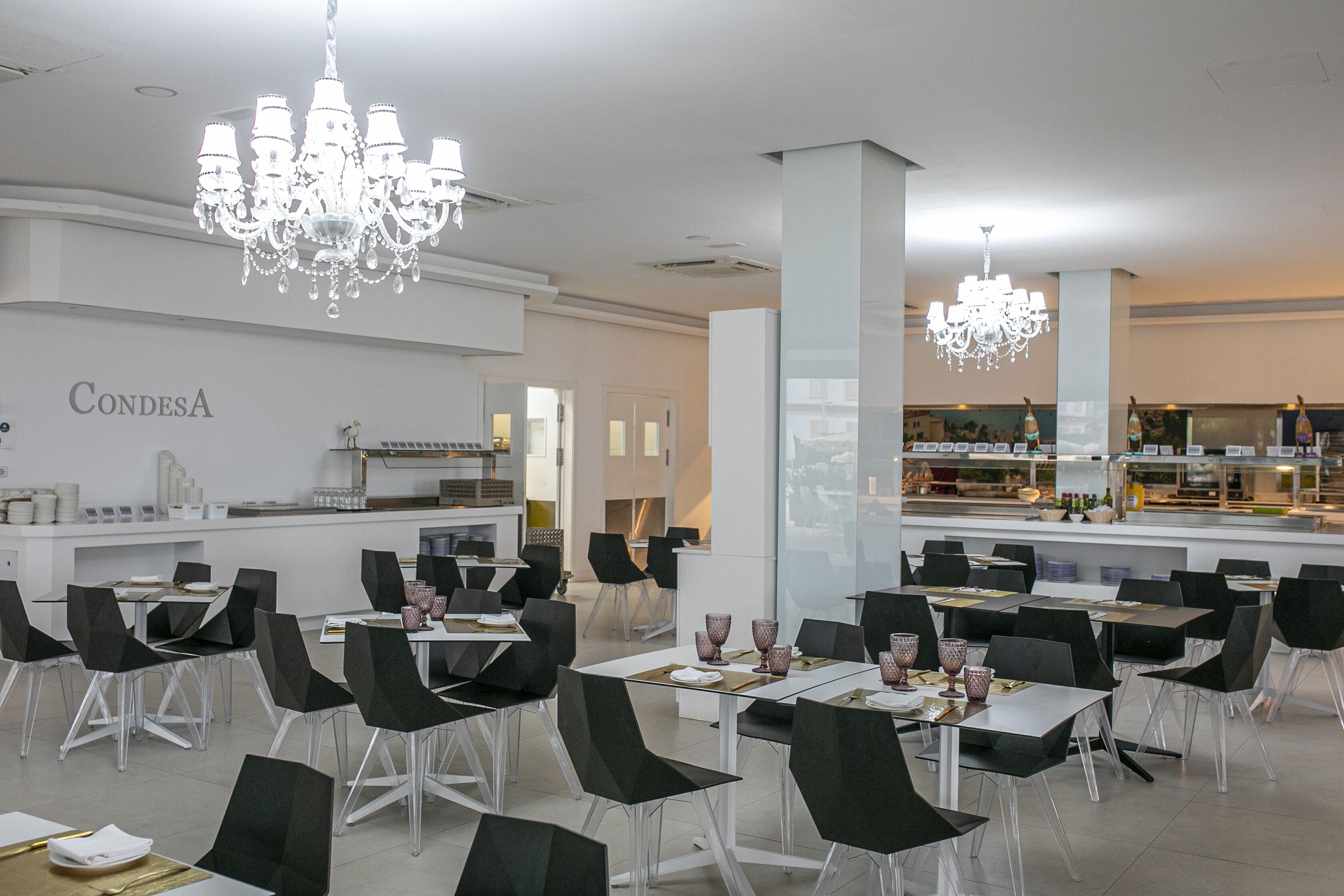 A modern restaurant interior with black chairs, white tables, and chandeliers.