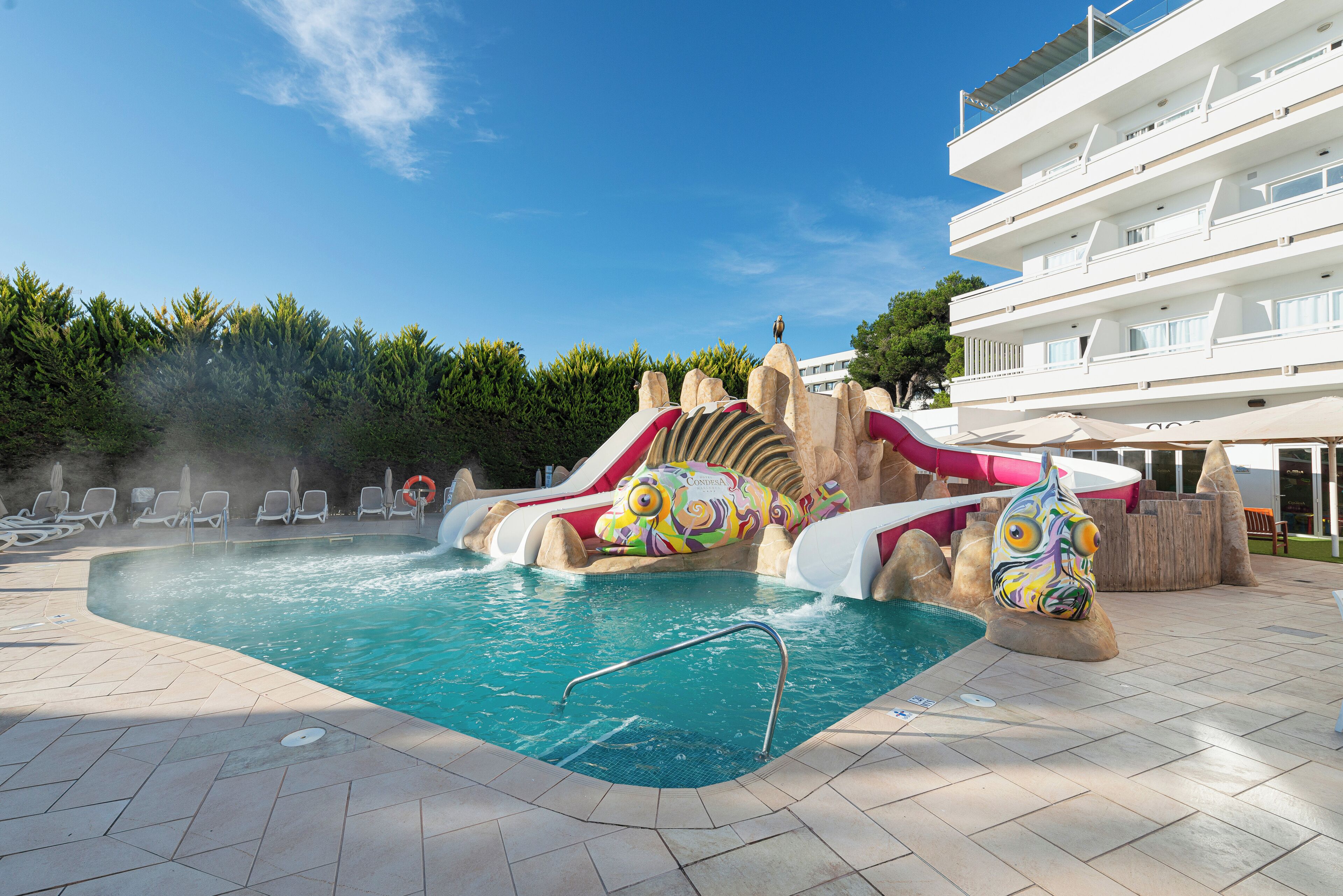 Une piscine avec un toboggan, des chaises longues et un poste de surveillance pour le sauveteur.