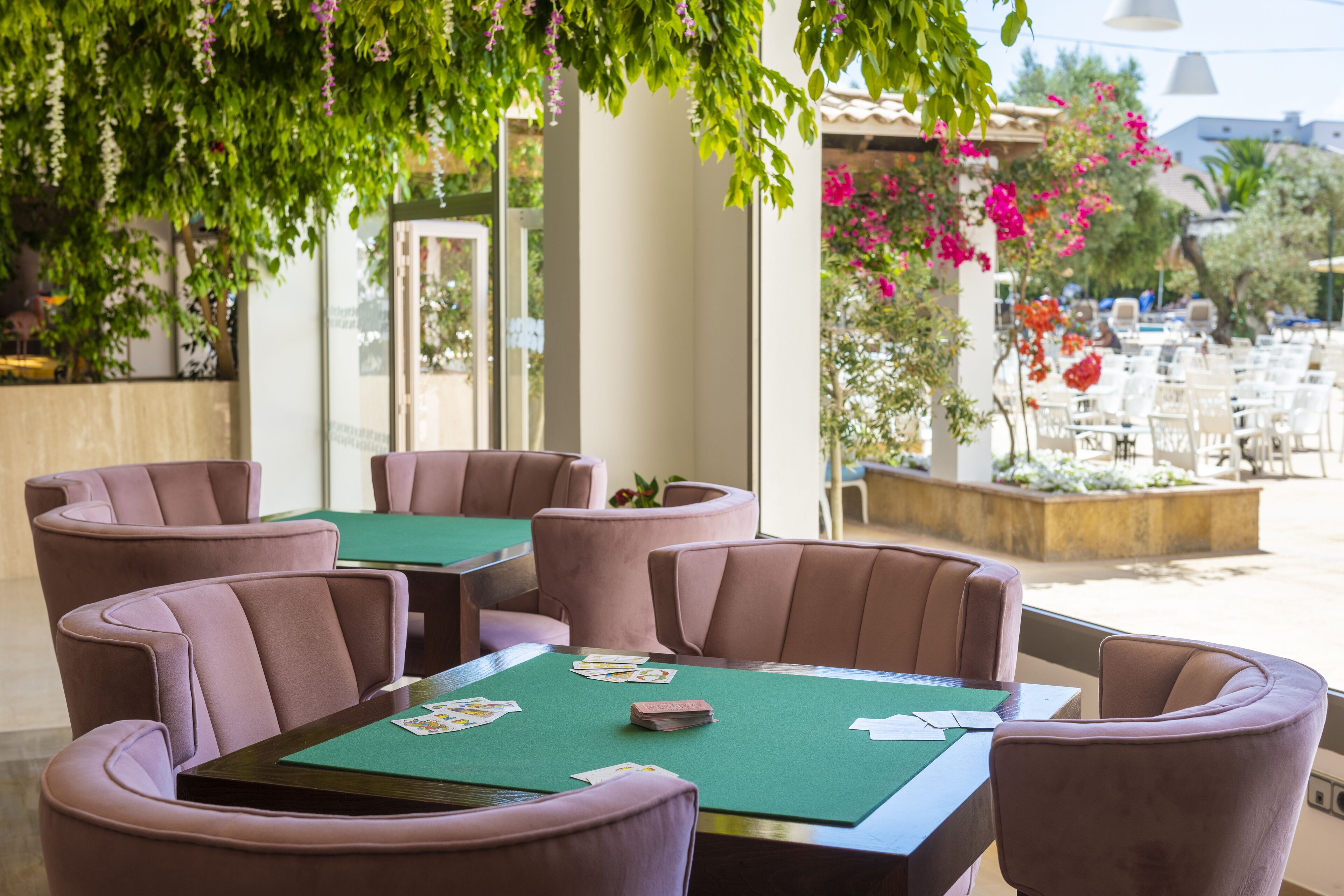 A casino table with green felt, surrounded by cushioned chairs, set outdoors with a view of other tables and chairs, and a building in the background.
