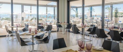 A modern dining area with tables and chairs, large windows, and a view of the ocean.