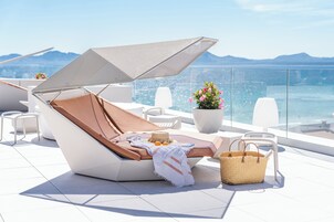 A modern outdoor lounge area with a cushioned chair, a large umbrella, and a potted plant.